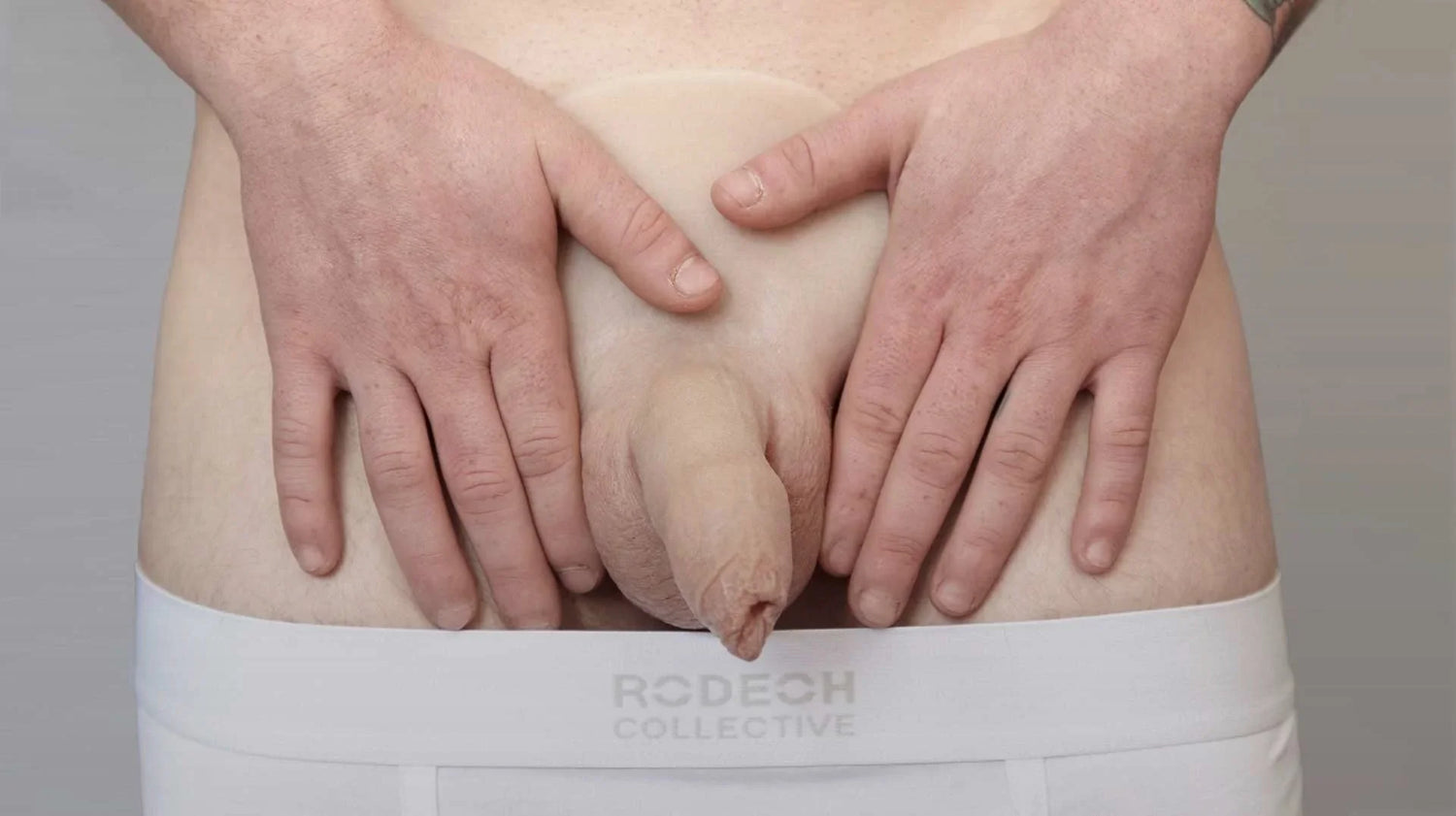 Transgender man wearing white underwear with realistic silicone FTM packer, hands resting on hips, showing natural skin detail.